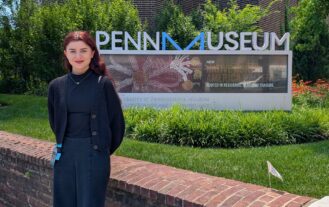 A woman stands outside in front of a sign that reads "Penn Museum".