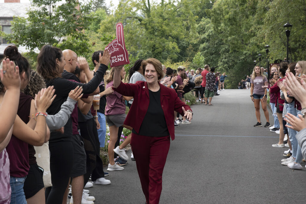 President Jebb walks up Mansion Road with a maroon foam finger on her right hand smiling with employees and families cheering