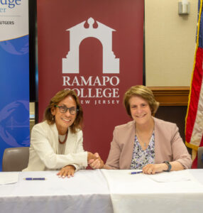 Deborah Visconi, CEO of Bergen New Bridge Medical Center shakes hands with Cindy Jebb, president of Ramapo College of New Jersey while seated at a table.