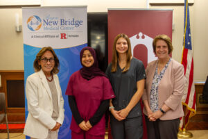 Standing in front of two banners displaying the Bergen New Bridge Medical Center and Ramapo College logos, from left to right: Bergen New Bridge President and CEO Deborah Visconi, Aamena Ismail BSN '29, Ava Picinic BSN '29, and Ramapo College President Cindy Jebb