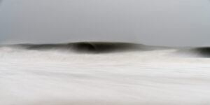 The black and white image shows a wave (no white caps) with beachline in the foreground