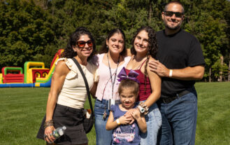 A family of 5 stands together outside. They are smiling.
