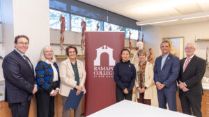 A group of seven people stand by a Ramapo College of New Jersey sign inside a lab.