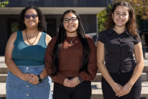 A group of three college students stand side by side.
