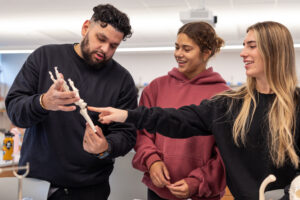 A professor shows two students a model of a hand.