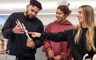 A professor shows two students a model of a hand.