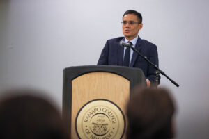A man in a suit stands behind a podium and speaks.