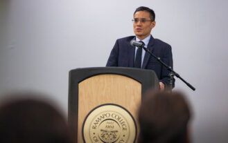 A man in a suit stands behind a podium and speaks.