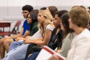 A group of college students sit in chairs, look forward and listen. 