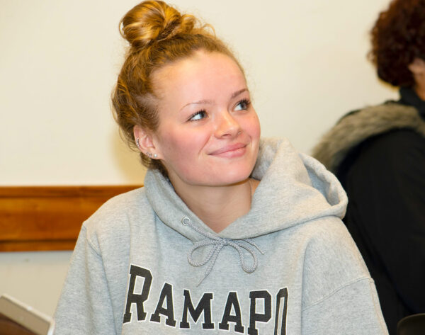 Ramapo College student wearing a gray Ramapo sweatshirt, smiling and looking off in the distance while in class