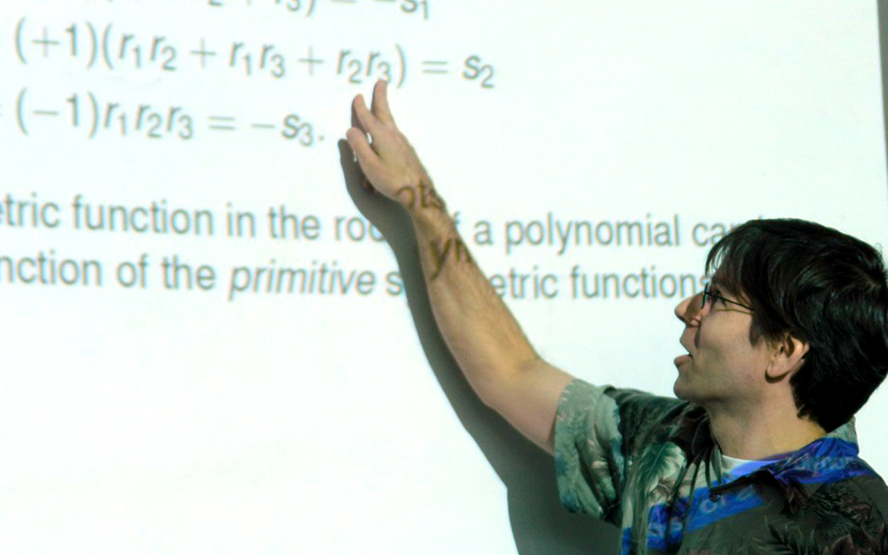 Professor pointing to math problems on a white screen