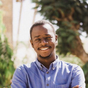Picture of film director Mamadou Dia standing outside on a sunny day, smiling.
