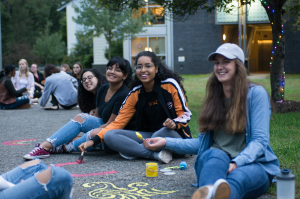 4 smiling students drawing with washable paint on a walkway