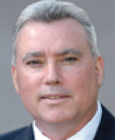 A man with gray hair in a collared shirt against a gray background.