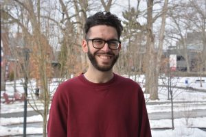 Luka stands outside in the Grove after a recent snowfall. He is posing for a photo and wears a maroon crewneck.