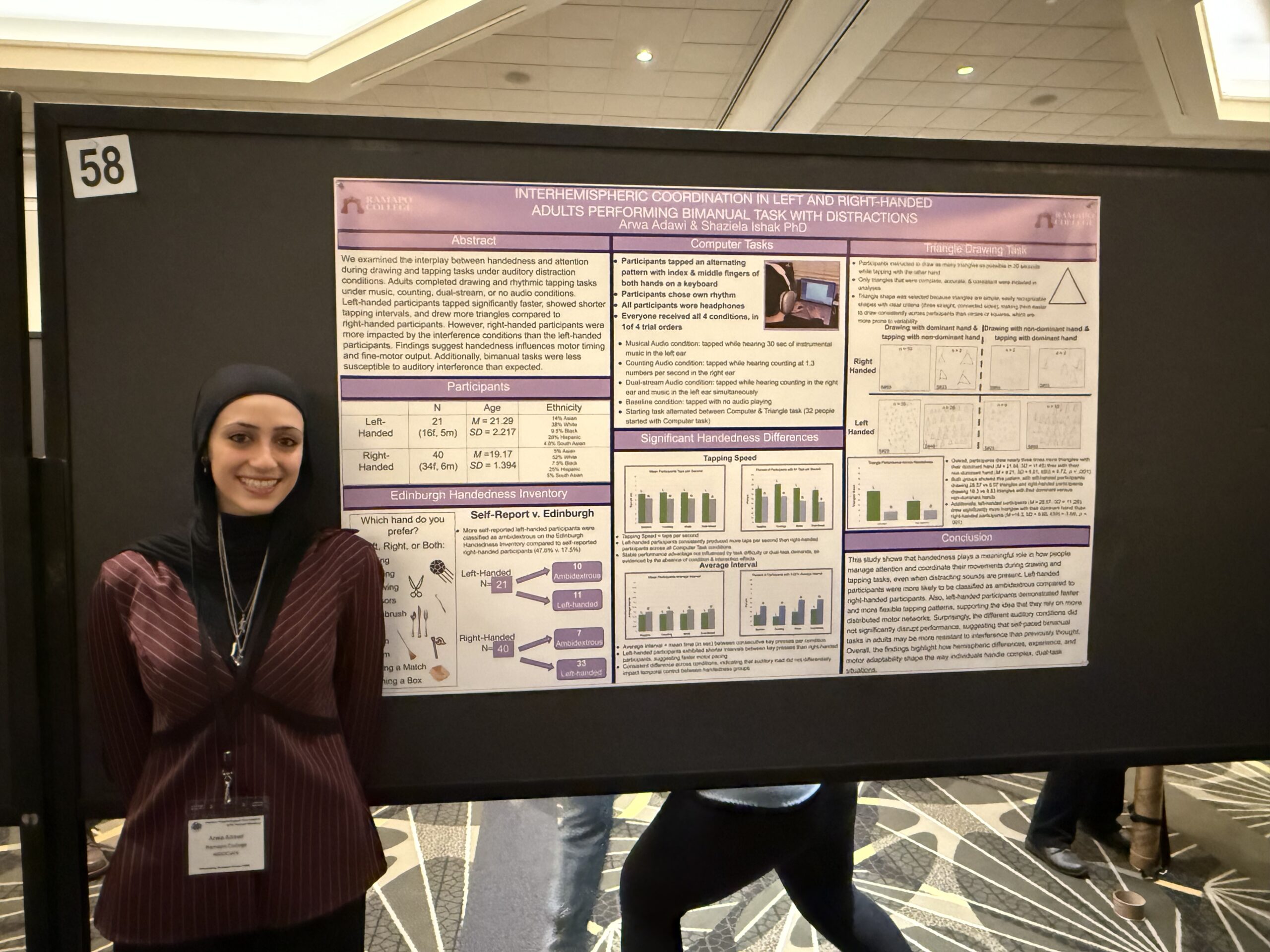 A woman in a black hijab and ID badge stands smiling beside a research poster titled Interhemispheric Coordination in Left and Right-Handed Adults Performing Bimanual Task With Distractions at a conference.