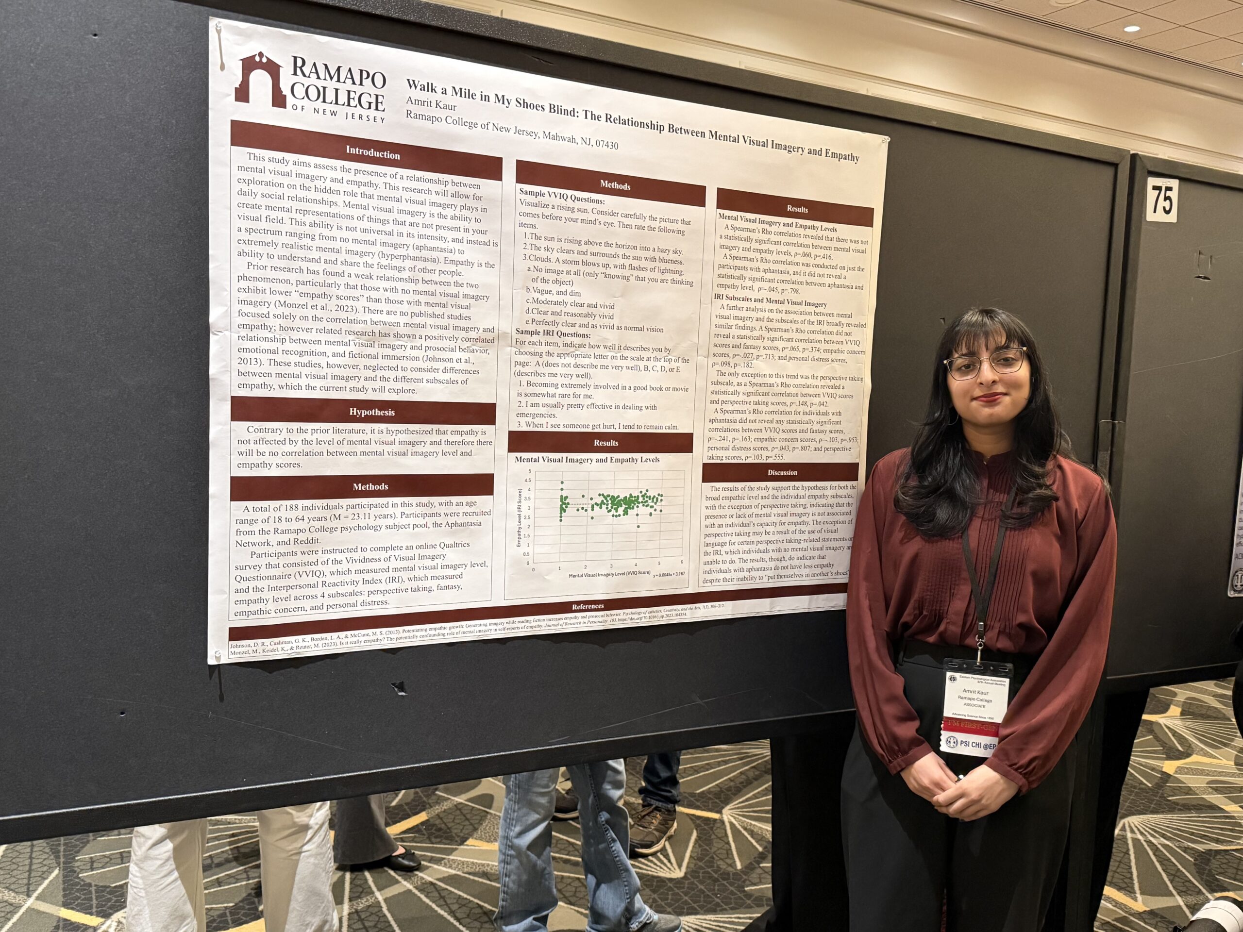 A young woman in a maroon blouse stands beside a research poster titled Walk a Mile in My Shoes Blind: The Relationship Between Mental Visual Imagery and Empathy at a Ramapo College event, displayed on a black partition.