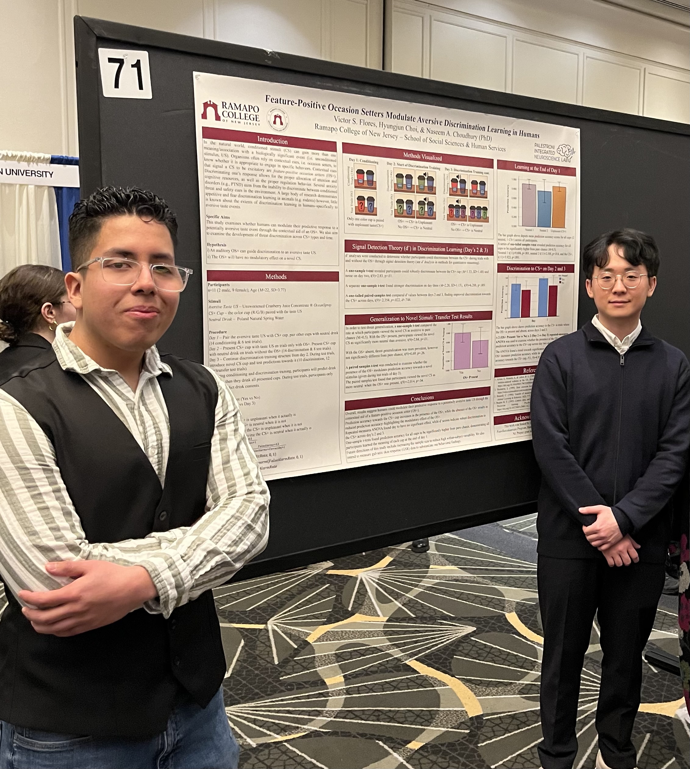 Two people stand in front of a scientific poster presentation labeled 71 at a conference. The poster displays graphs, text, and images with the Ramapo College logo visible at the top left corner.