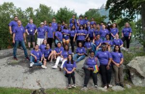 A group of students wearing purple t-shirts smiling outside