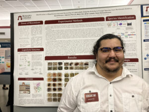 Student posing in front of their research poster.