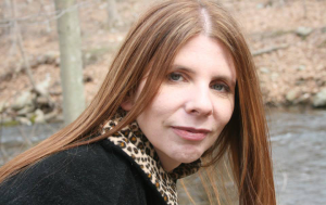 Ramapo Success Story - headshot of a woman, wearing black sweater with leopard print around the neck. Behind her are woods