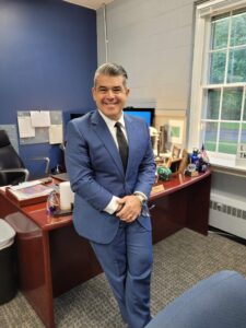 Adam Fried standing in his office at Ramapo College, leaning on his desk and smiling