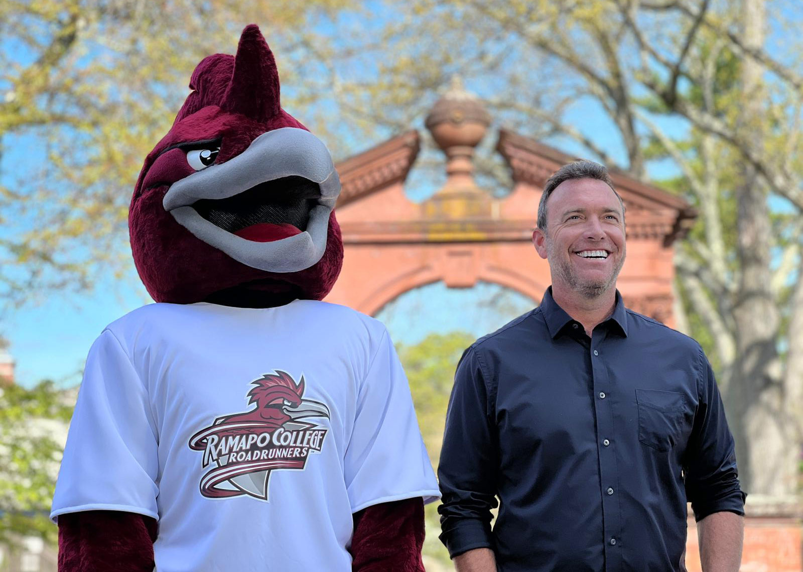 Alex Boylan and Ramapo College's Roadrunner mascot standing together outside of the Havemeyer Arch 