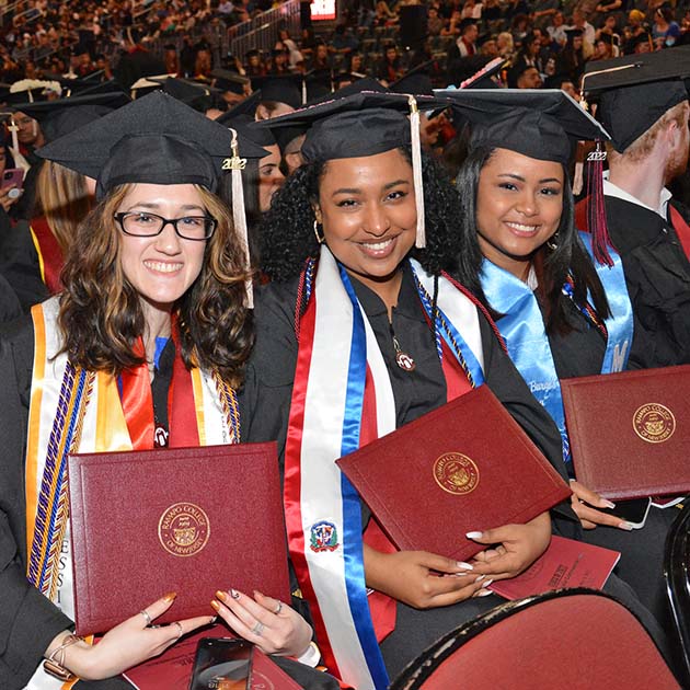 Three students wearing regalia holding their diplomas