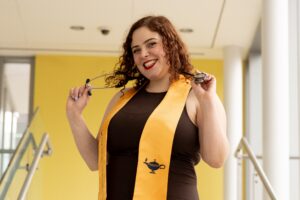 Anna smiles while wearing a yellow nursing graduation stole and holding her stethoscope around her neck.