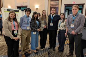 Dr. Dasgupta stands in front of a student research poster at the ECA conference. To the left of her is Sara Hosbach and Joseph Bennis To the right of her is Kaitlyn Camerlengo, Joseph Santana, Melissa Glasson, and William Jackson.