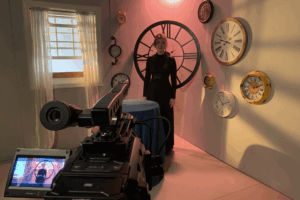 A video camera points toward a woman in a black dress.